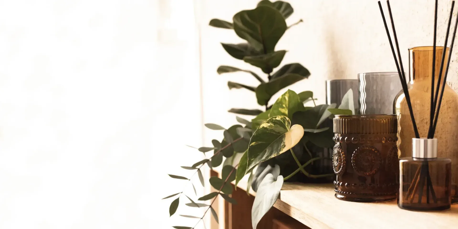 A worn light-oak surface in warm light with folded linen, dried greenery in a stoneware vessel, and smooth travertine stones