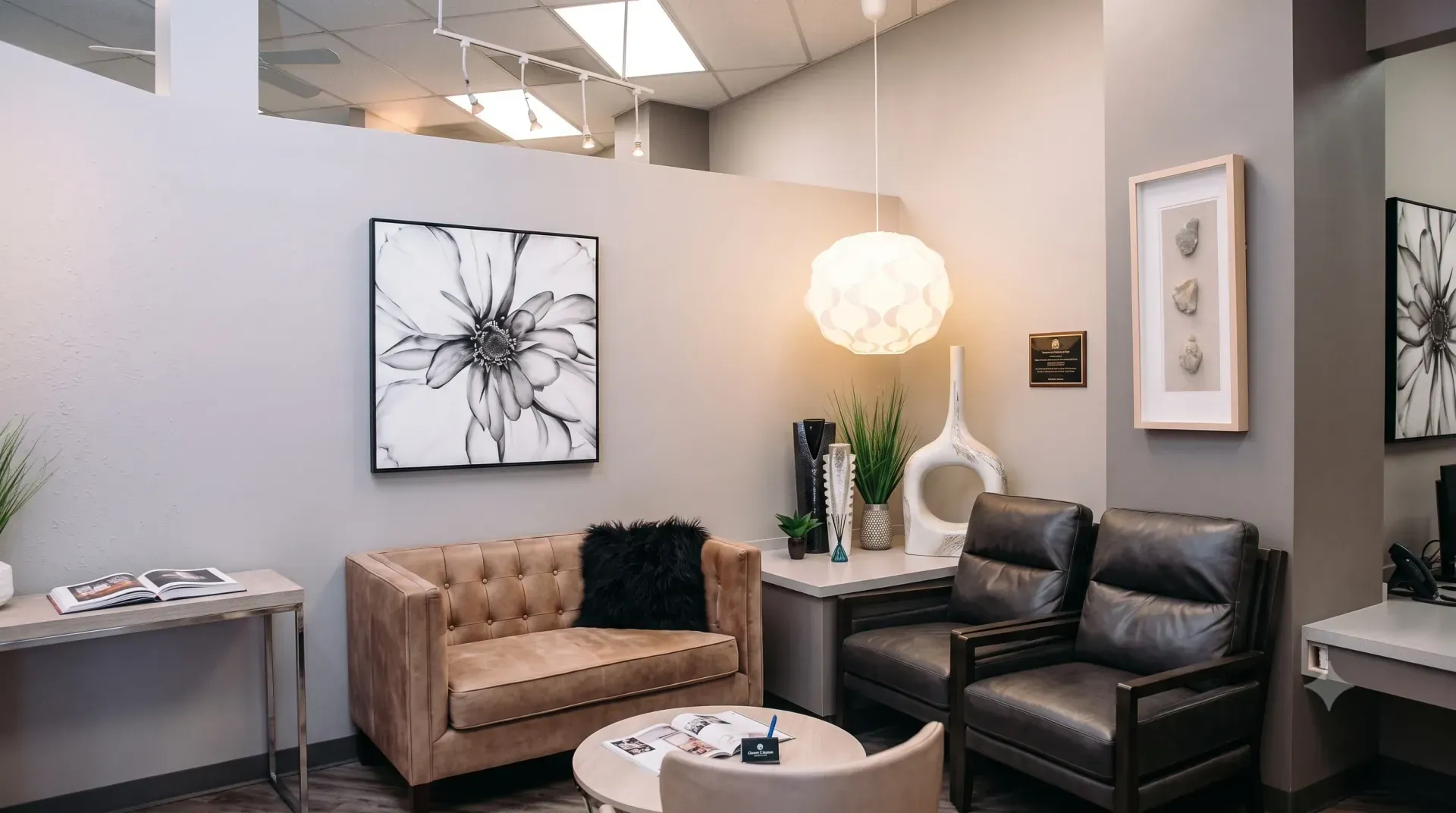 The Salon 695 reception seating area with a tan leather sofa, soft pendant light, and framed botanical prints
