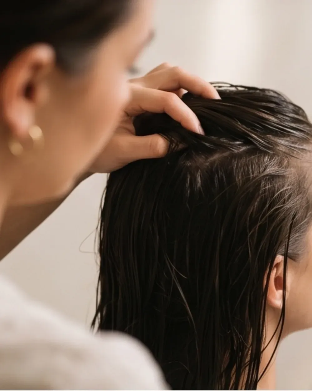 A stylist working a treatment through a client's damp dark hair at the scalp